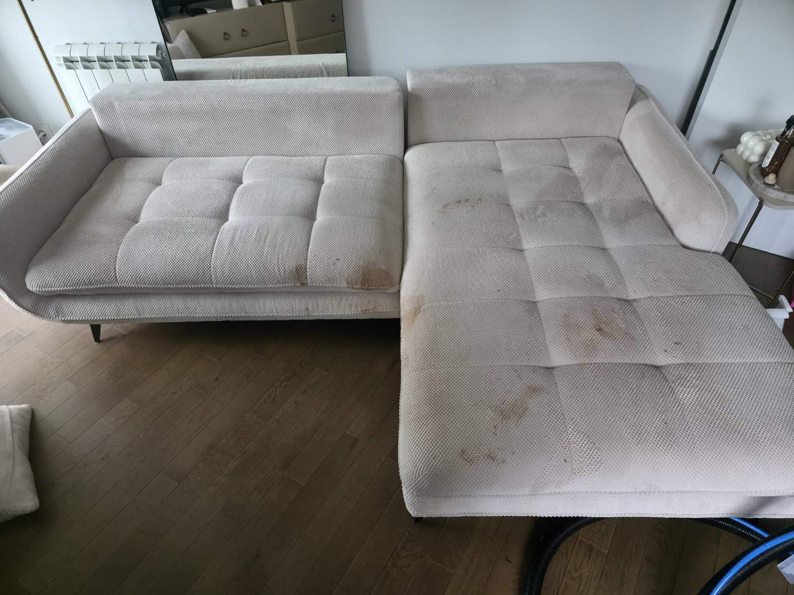 Light beige sectional sofa with visible brown stains on cushions and chaise lounge in a living room.